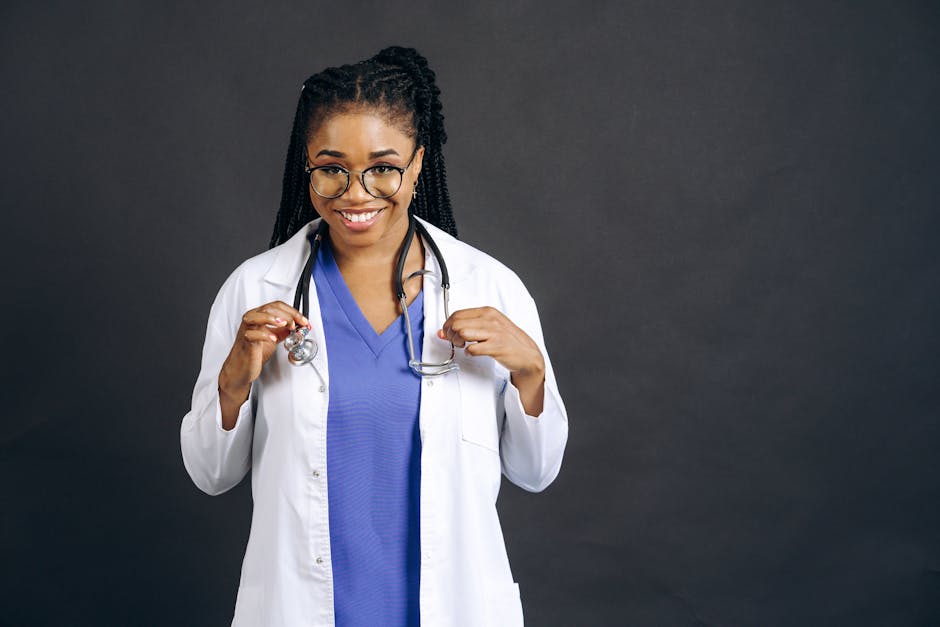Portrait of a smiling female doctor wearing eyeglasses and a lab coat against a gray background.