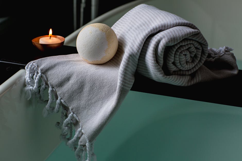 Serene spa scene with a lit candle, bath bomb, and towel on the bathtub edge